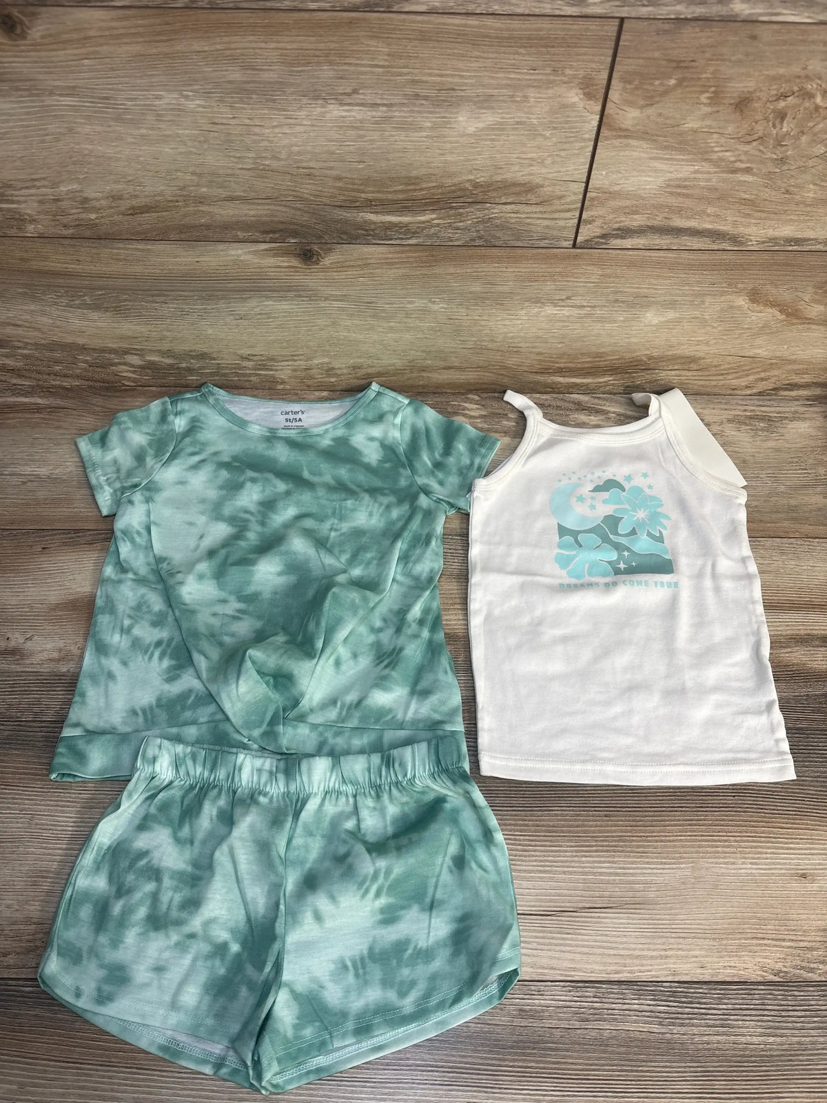 Green tie-dye toddler shorts set and white tank top with blue graphic on wood floor