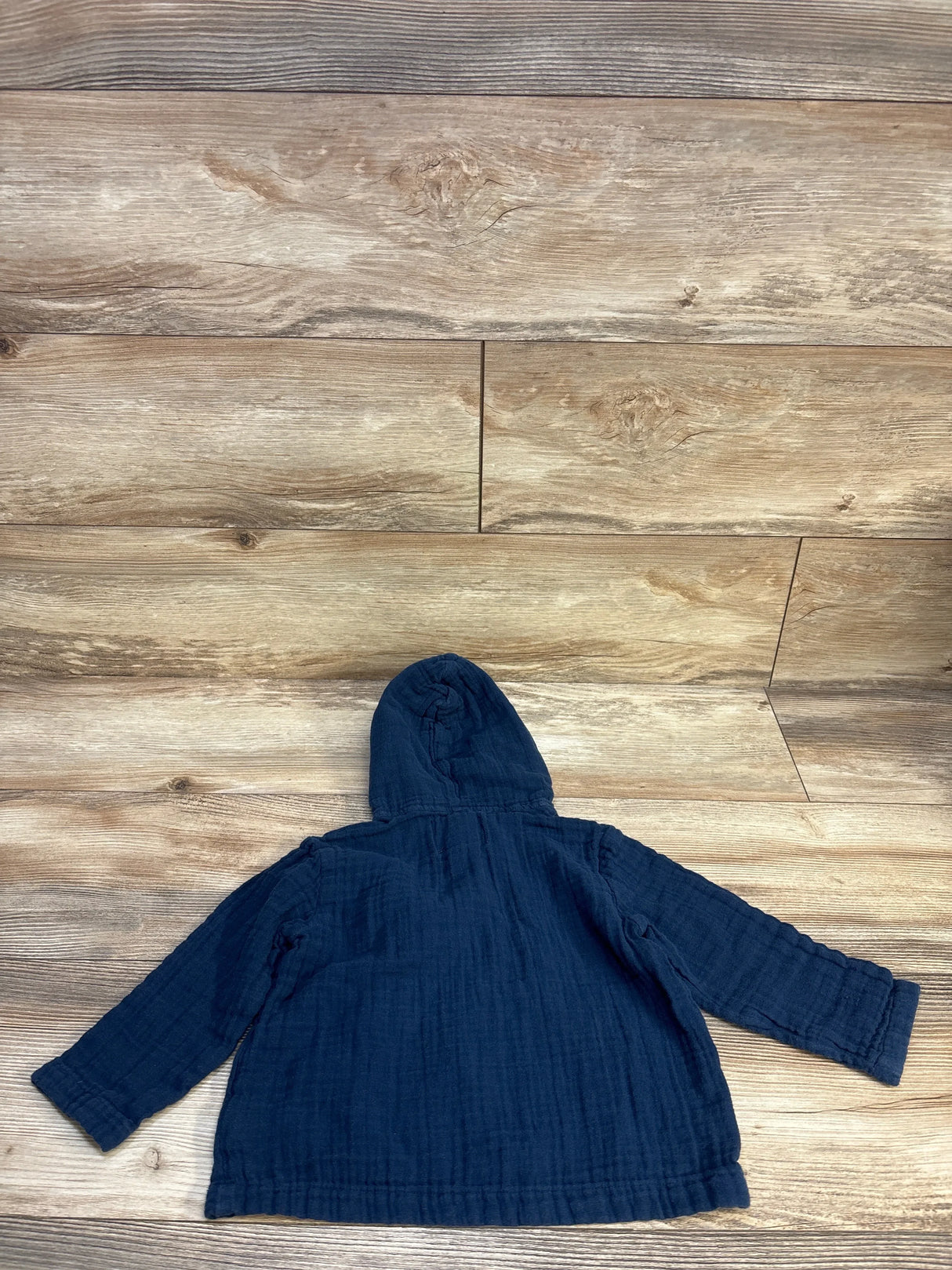 Flat lay of Old Navy gauze pullover hooded shirt in navy with long sleeves and hood up on wood plank floor