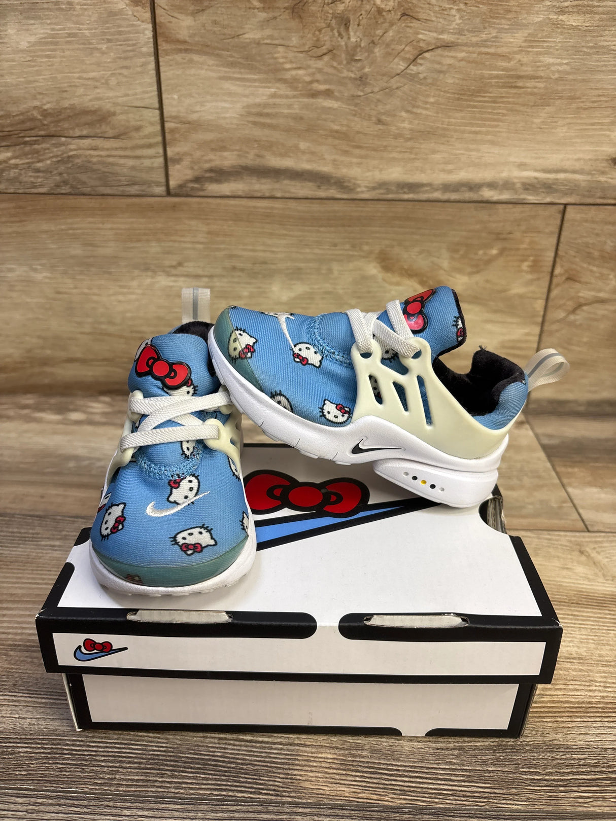 Front and side view of Hello Kitty x Nike Air Presto sneakers size 7C, blue Hello Kitty print, white cage lacing on wood floor