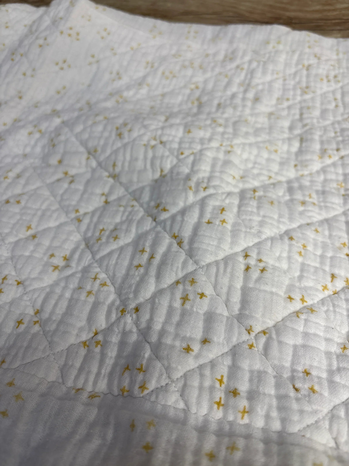 Close up of organic cotton changing pad cover showing white fabric with small yellow star print and quilted diamond stitching