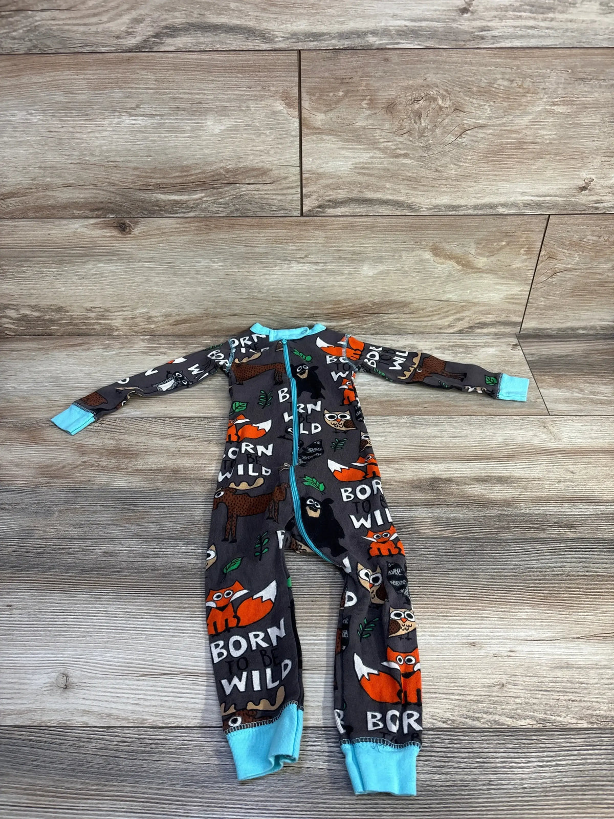 Flat lay of grey Born to Be Wild infant sleeper showing fox and owl print and teal zipper and cuffs on wood floor