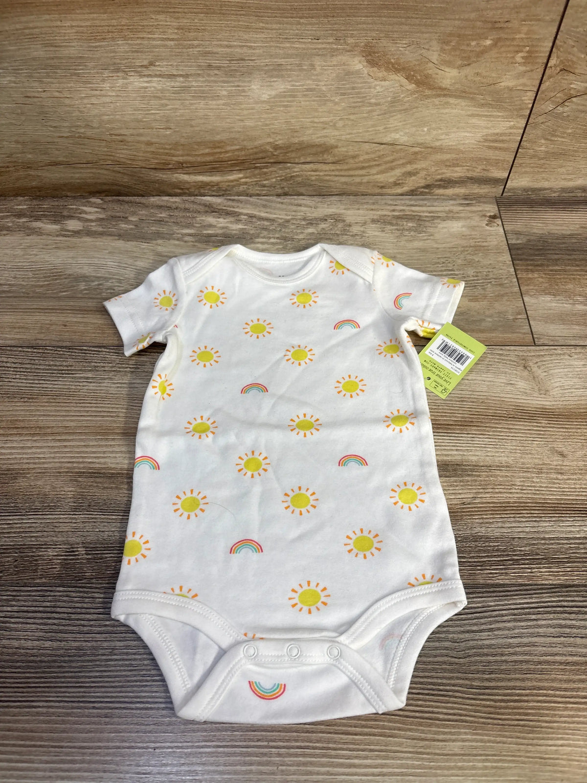 Front view of Primary sun print bodysuit in white showcasing short sleeves and snap closures with a wood floor background