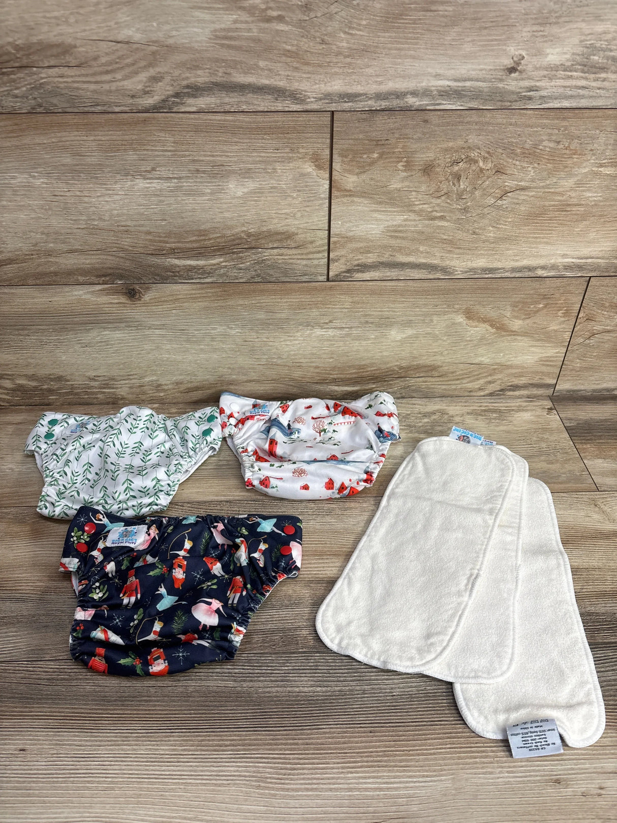 Top-down view of Rig 'N Gigs pocket cloth diapers 3-pack showing three printed covers and two white absorbent liners on wood floor