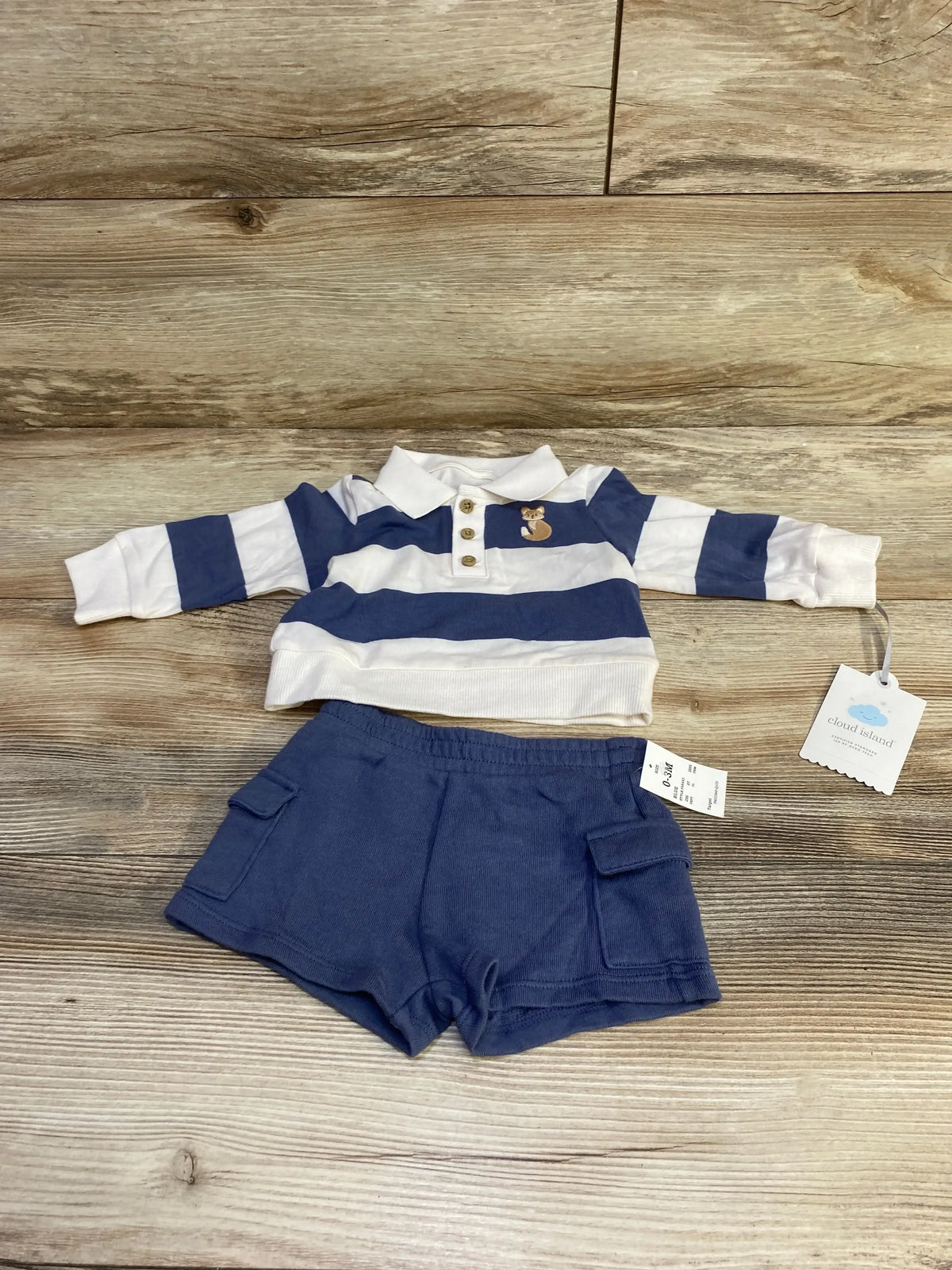 Flat lay of Cloud Island baby polo and shorts set with blue and white stripes, fox chest patch, and cargo shorts on wood