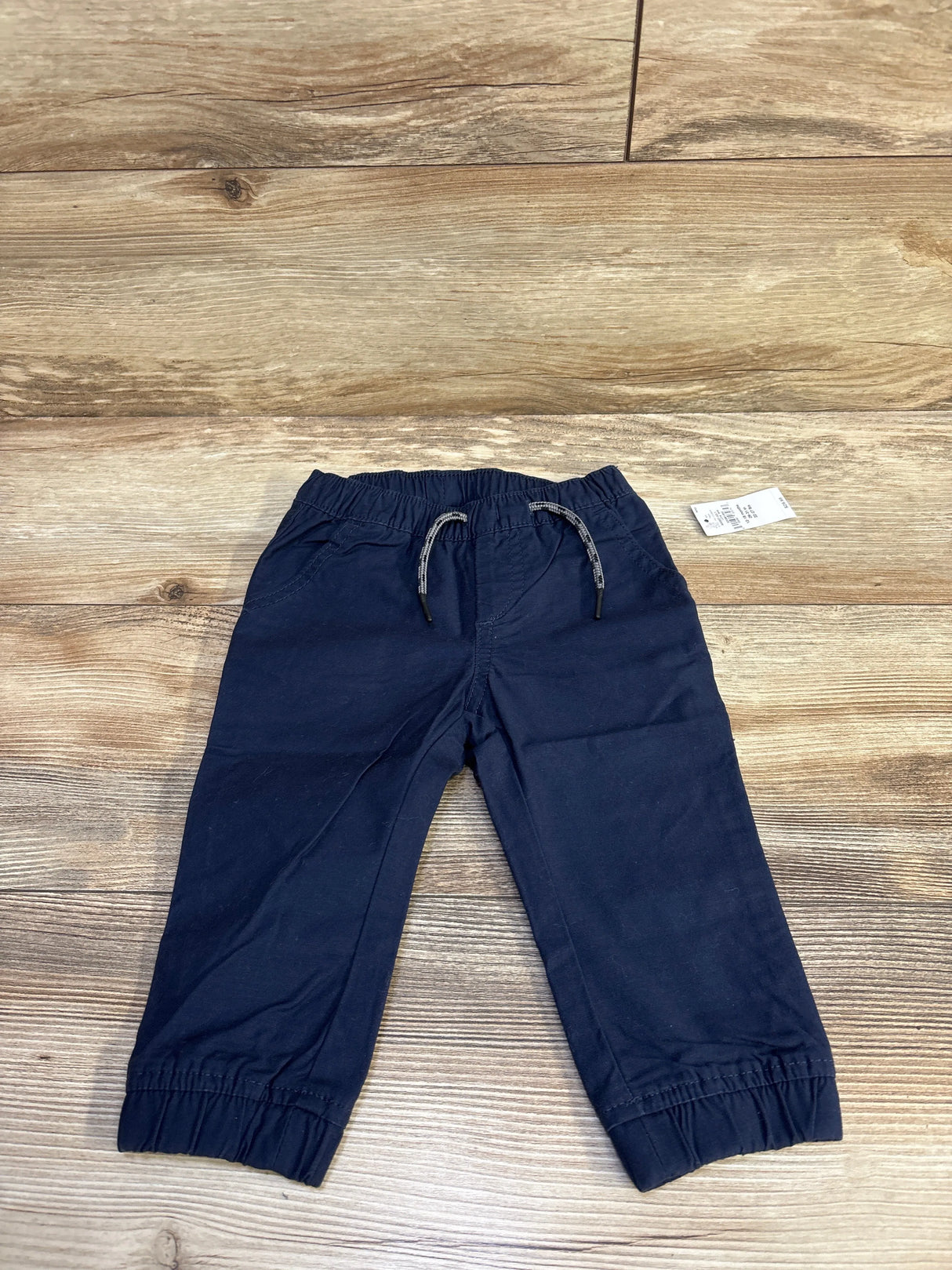Flat-lay of Baby Gap navy drawstring joggers, size 12–18 months, showing elastic ankle cuffs and drawstring waist on wood floor