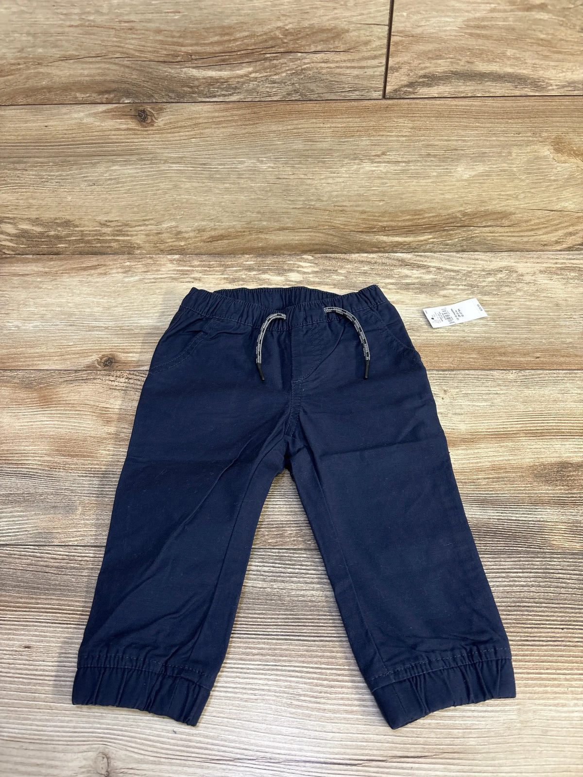Flat-lay of Baby Gap navy drawstring joggers, size 12–18 months, showing elastic ankle cuffs and drawstring waist on wood floor