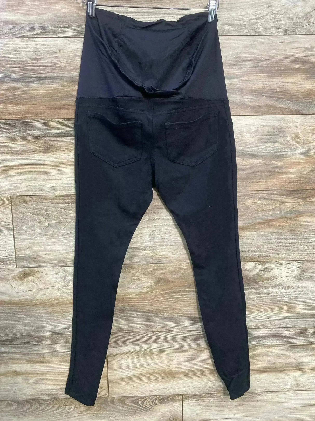 Back view of Isabel maternity crossover panel pants, black, showing crossover belly panel and back pockets on wood floor