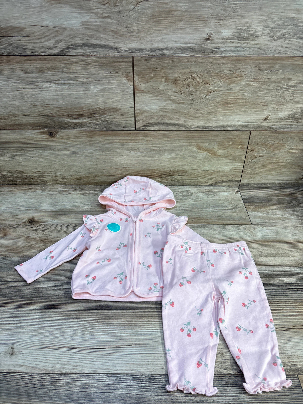 Flat lay of pink Child of Mine strawberry zip-up hooded jacket and matching pants showing ruffled shoulders on wood floor