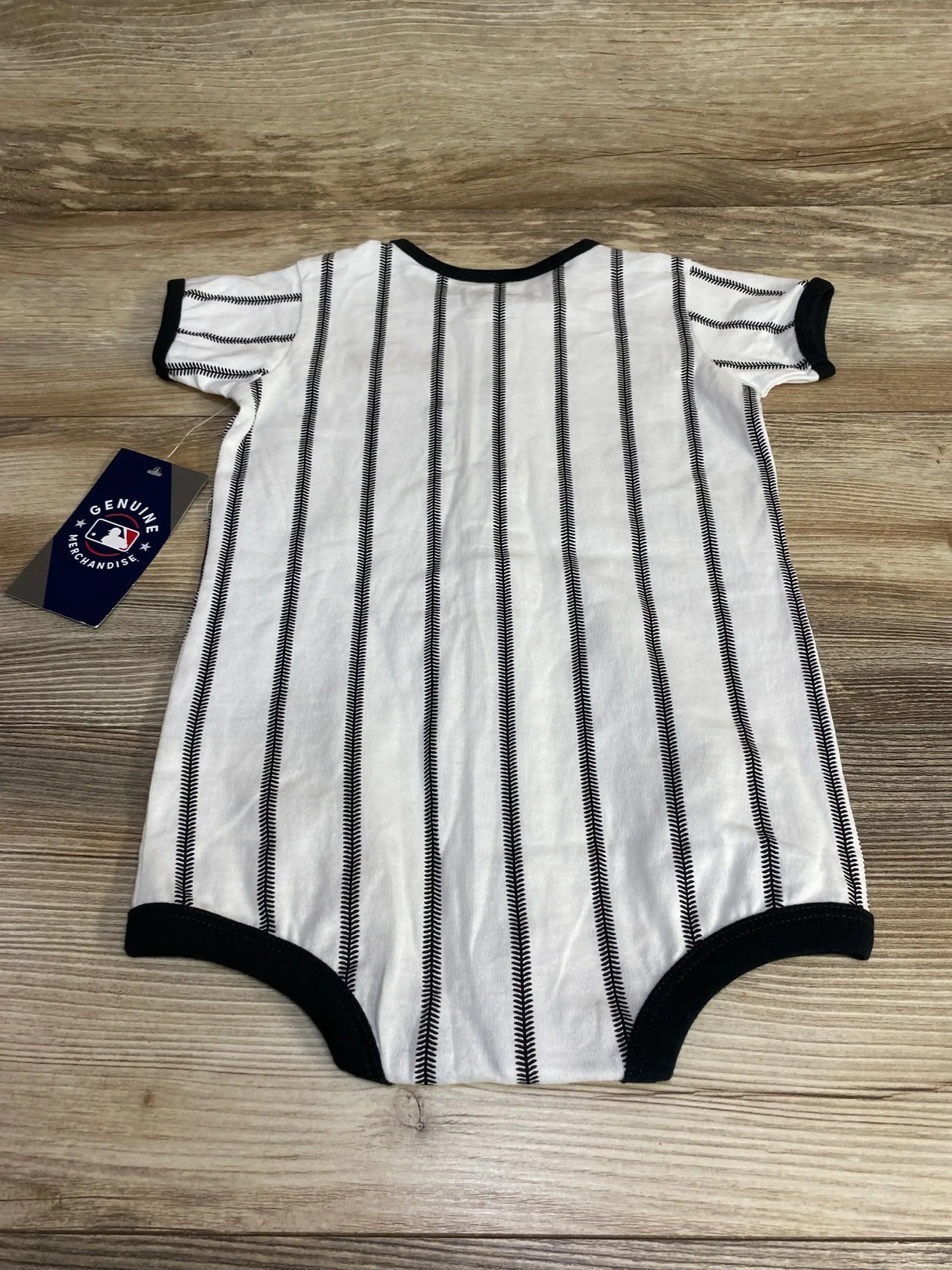 Flat lay of white baby San Francisco Giants pinstripe romper showcasing vertical black stitch stripes, black trim and MLB Genuine Merchandise hang tag on wood background