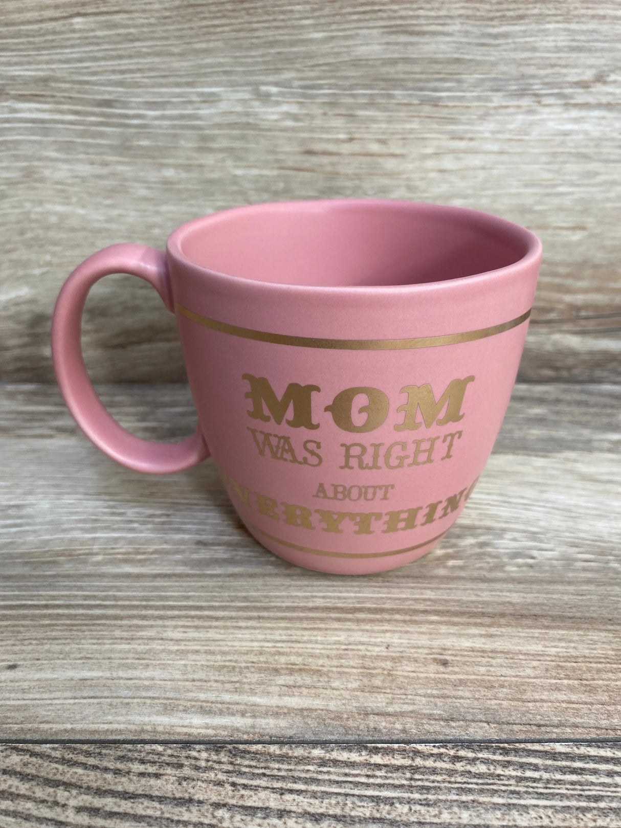 Side view of NEW Stoneware Mom Was Right About Everything Mug in pink showcasing matte pink ceramic finish with gold text on wood plank floor