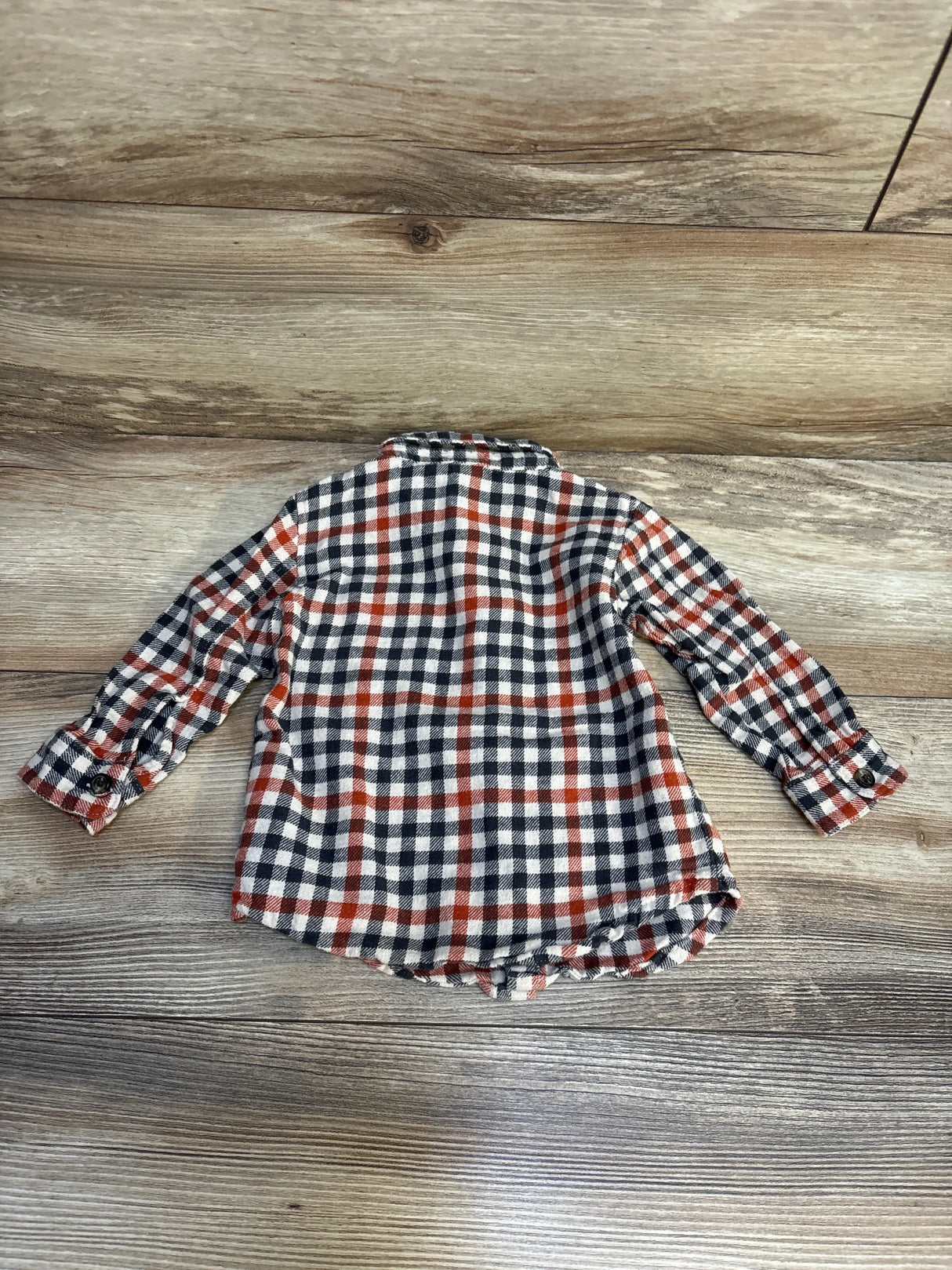 Kids long sleeve plaid shirt with red, black, and white check pattern on wood floor