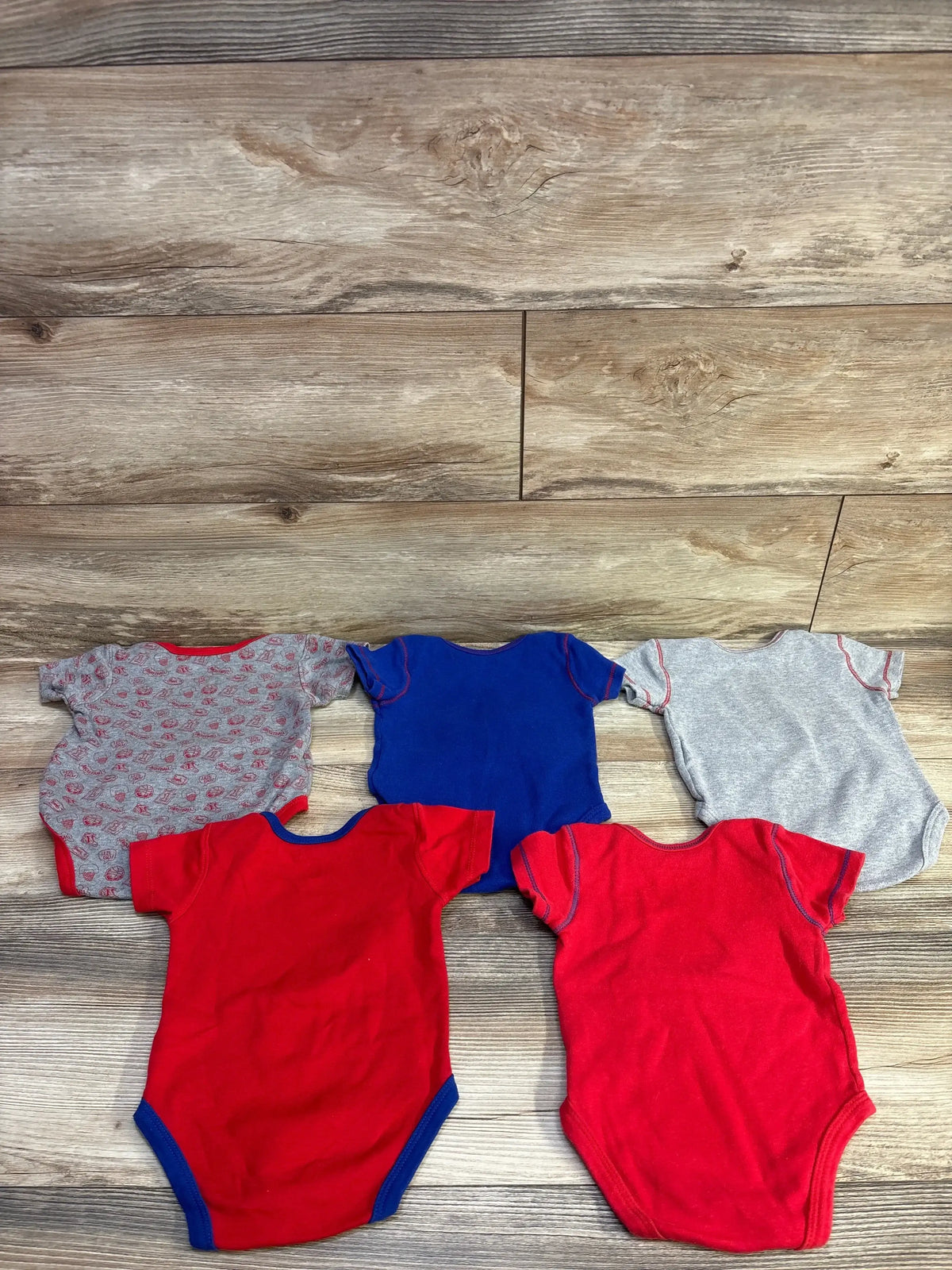 Top-down view of five Clippers basketball bodysuits in blue, red, and gray, showing short sleeves and bottom snap closures