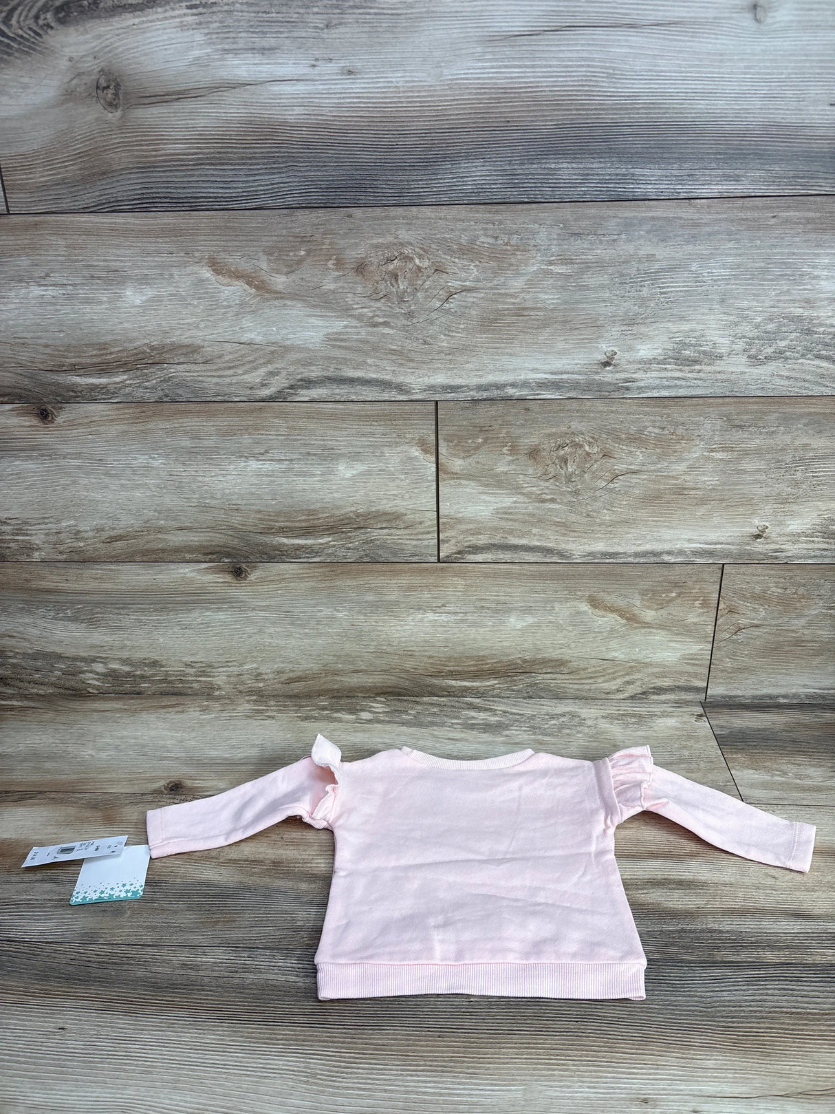 Light pink long sleeve baby shirt with ruffle shoulders on wood background