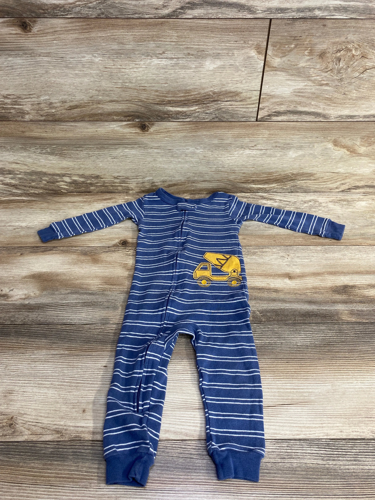 Blue and white striped baby onesie with yellow construction truck patch on wooden floor