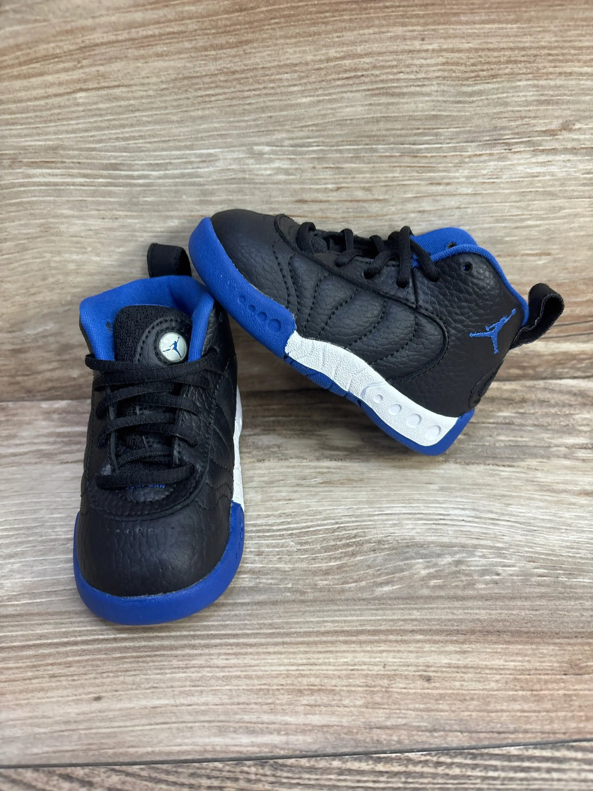 Front and side view of toddler Air Jordan Jumpman Pro BT sneakers showing black leather, blue accents, Jumpman logo on wood