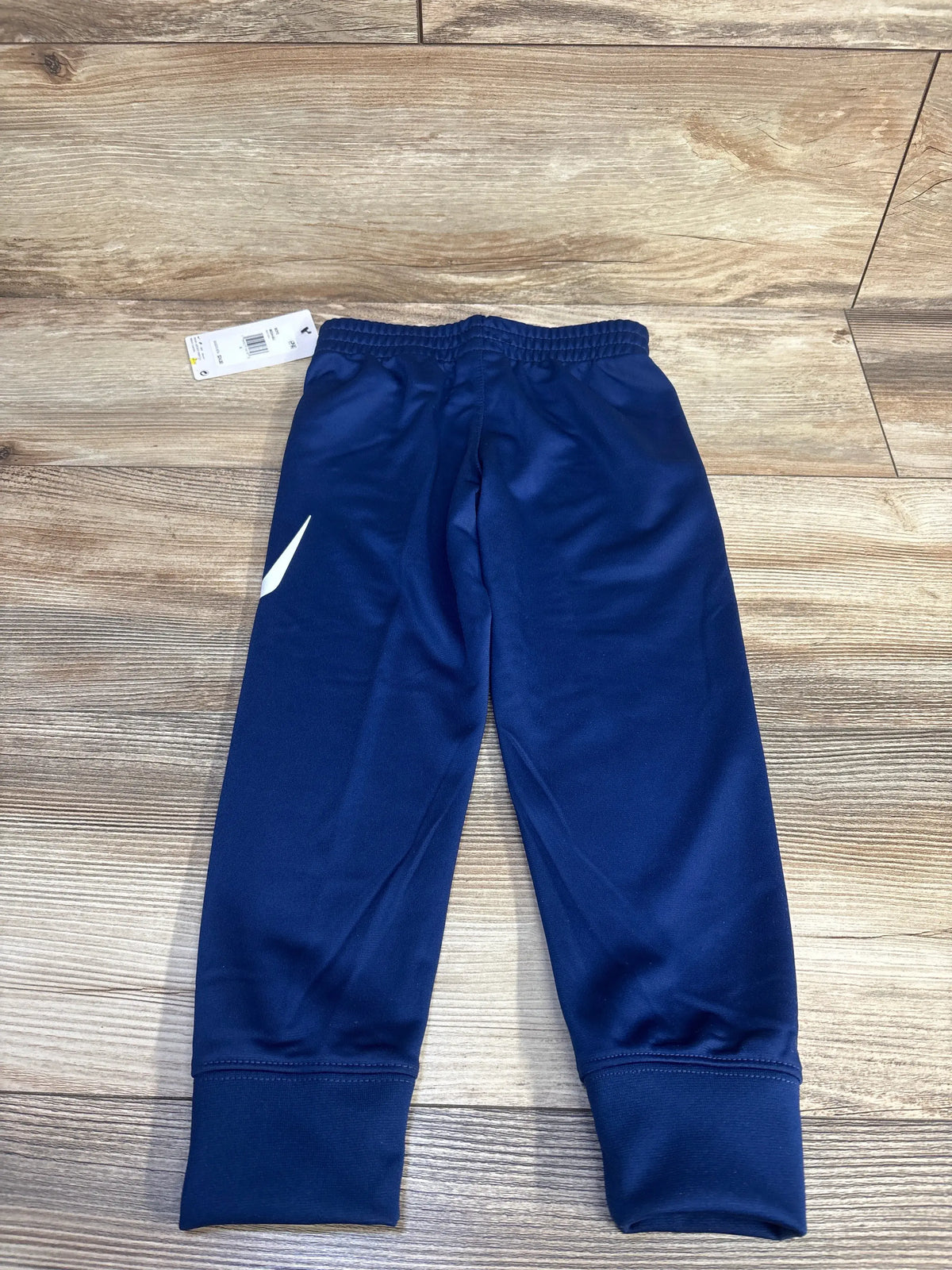 Front view of Nike Dri-Fit joggers, blue size 4T, showcasing elastic waistband and ankle cuffs on wood floor
