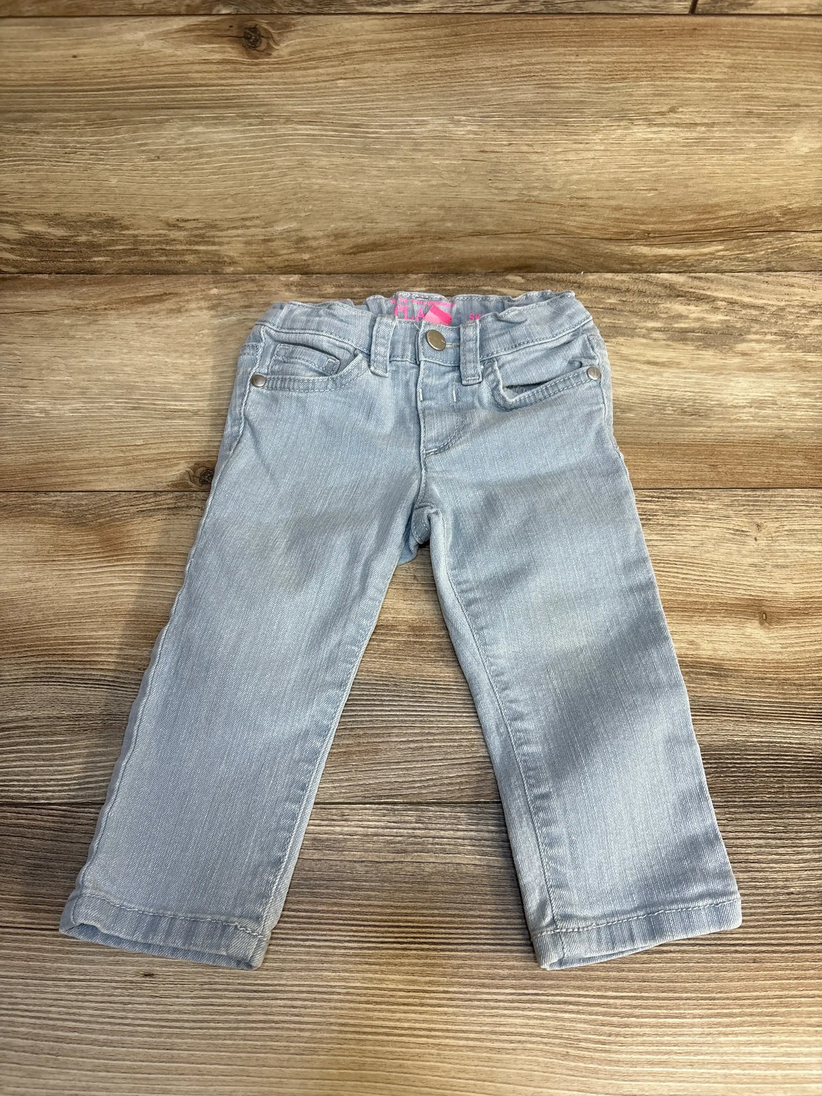 Flat lay of Children’s Place light blue toddler jeans, size 12–18 months, showing elasticized waist, front pockets, and pink brand tag on wood floor