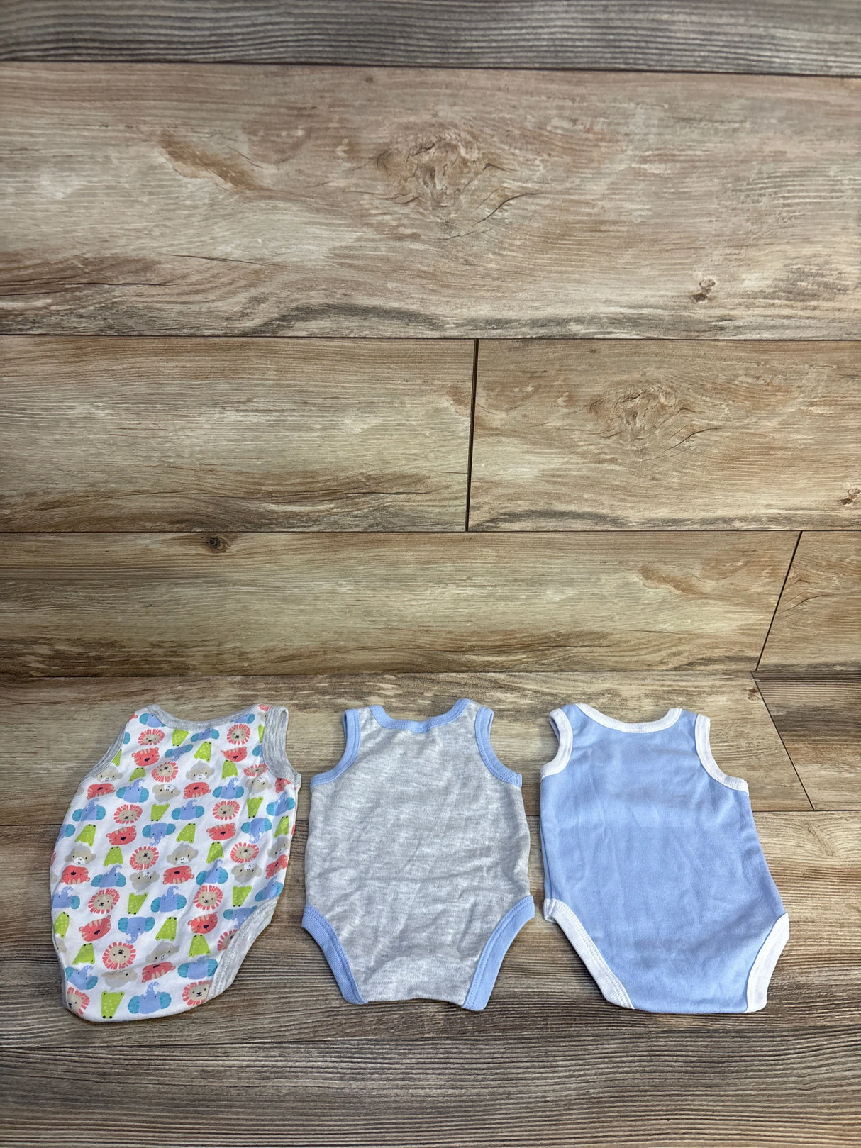Three sleeveless baby bodysuits in floral, gray, and blue designs on a wood background