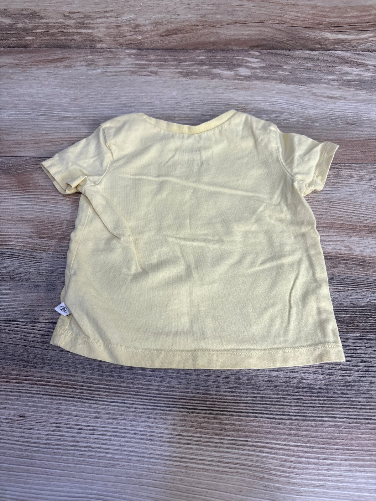 Front view of Honest Baby solid yellow shirt showcasing short sleeves and crew neckline on a wood-grain background
