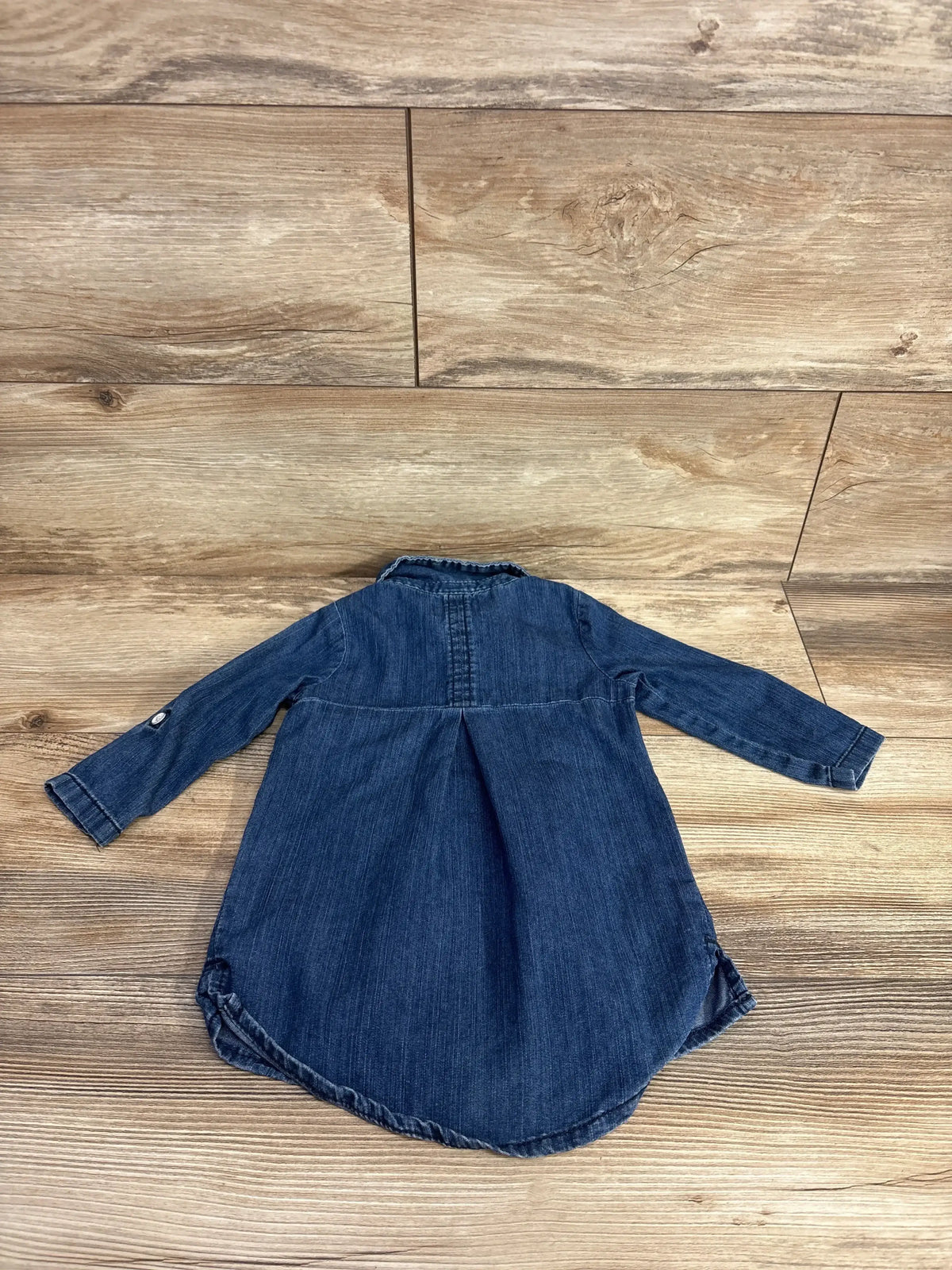 Back view flat lay of long sleeve denim toddler shirt dress with high low hem and pleated back yoke on wood plank floor