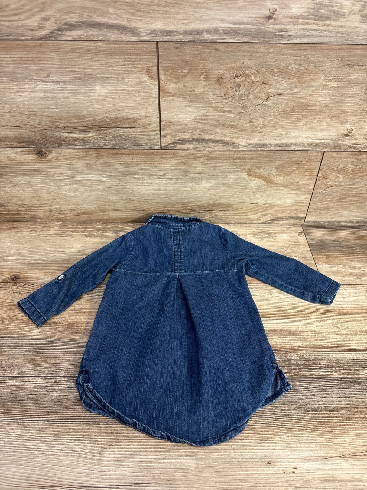 Back view of a long sleeve denim toddler dress on wood background