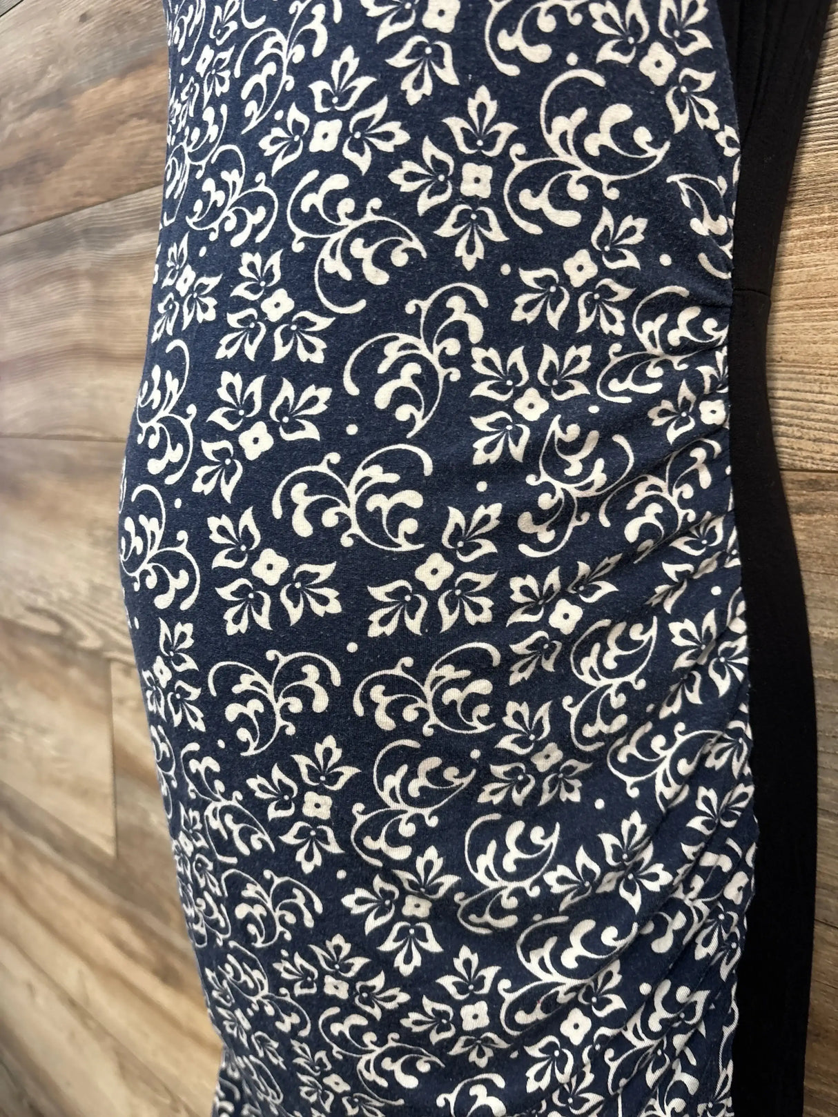 Side close-up of Kimi + Kai tank floral maternity dress in black showing white floral print and ruched side on wood floor