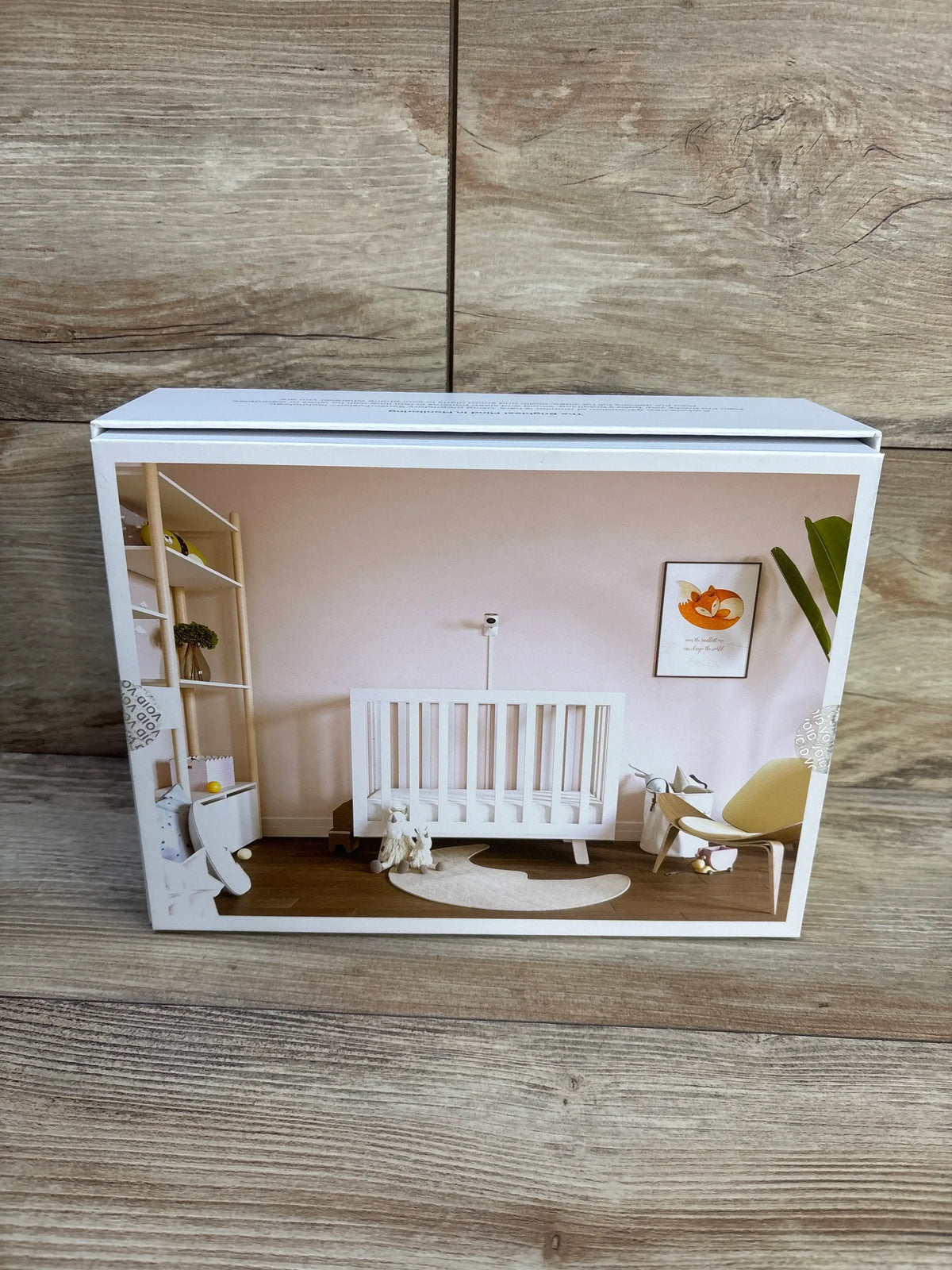 Front view of Miku Pro Smart Baby Monitor with wall mount kit, packaged box showing nursery scene on wooden floor