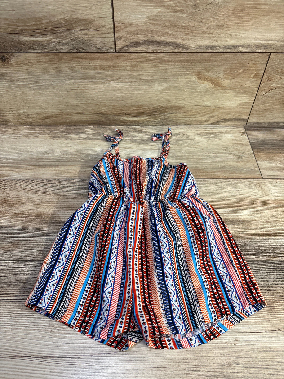 Flat lay of toddler tank romper with multicolor tribal stripes, tie shoulder straps and elastic waist on wood floor