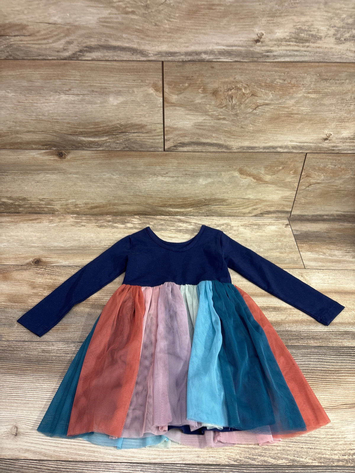 Hanna Andersson long sleeve navy blue dress with a rainbow tulle skirt on a wood background