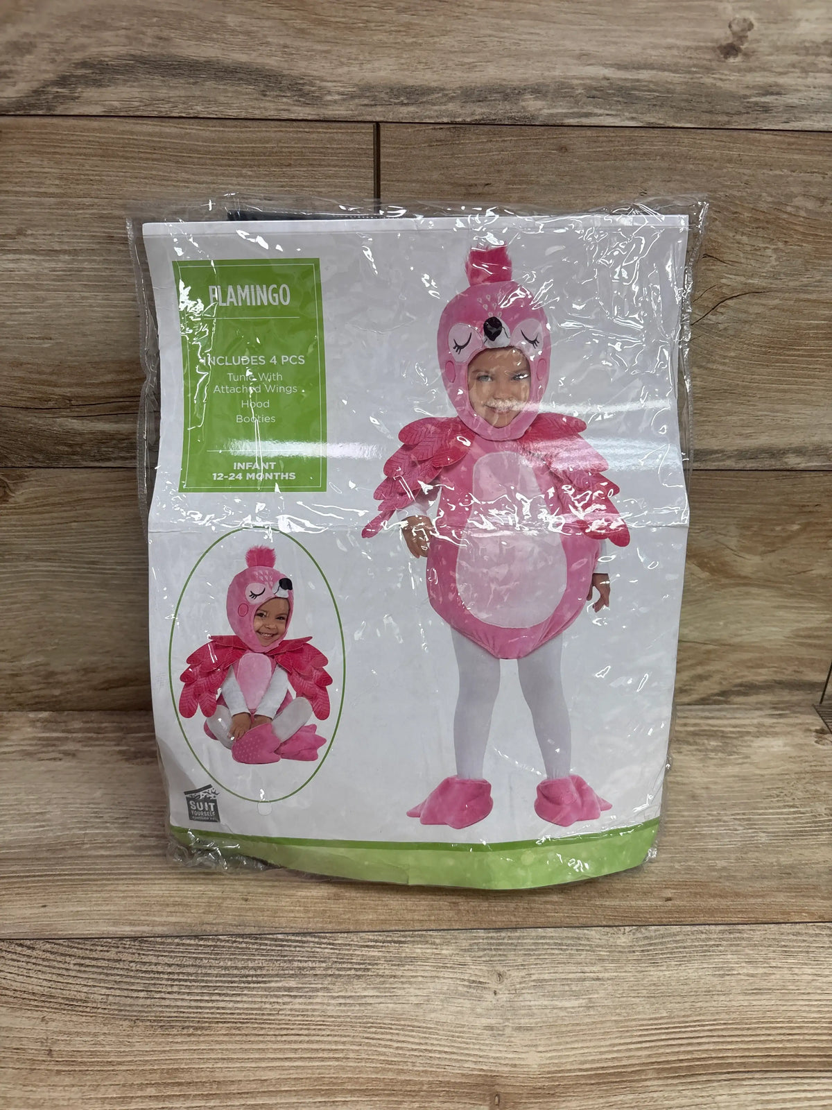 Front view of pink flamingo costume package showing hood, attached wings, and booties on a wood background