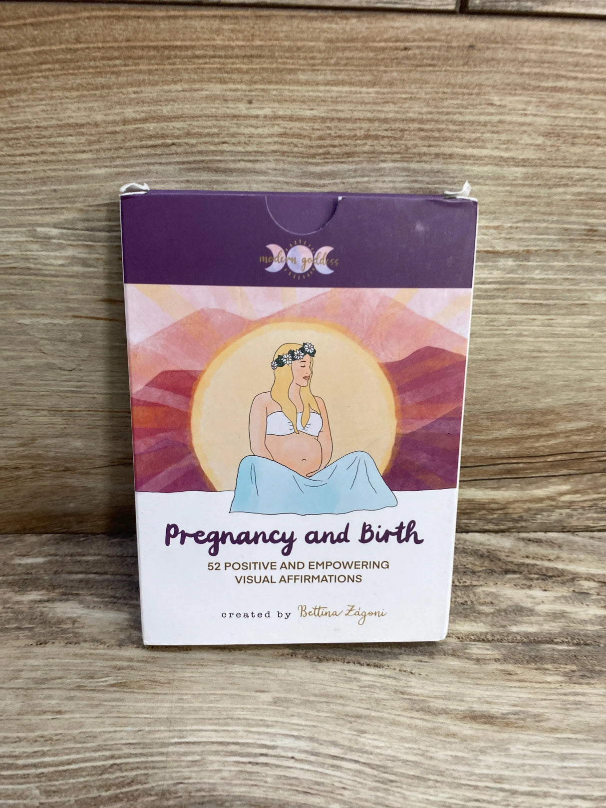 Front view of Pregnancy and Birth 52-card affirmation box showing illustrated pregnant woman and title with a wood tabletop background