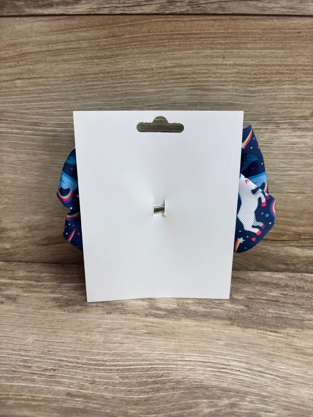 Back view of NEW Large Unicorn Hair Bow Blue showcasing blank white card with blue unicorn print bow peeking from behind on wood plank background