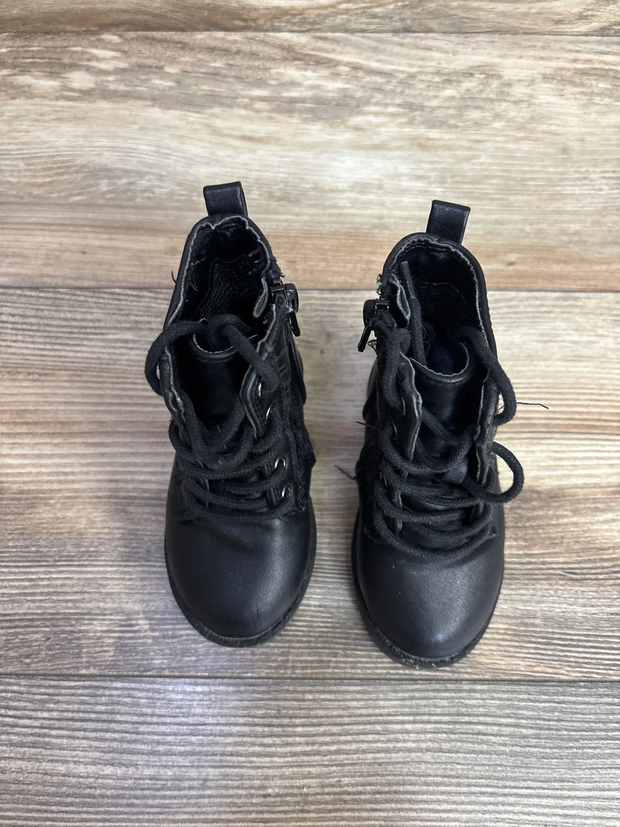 Pair of black toddler boots with laces and zippers on wooden floor in kids resale store