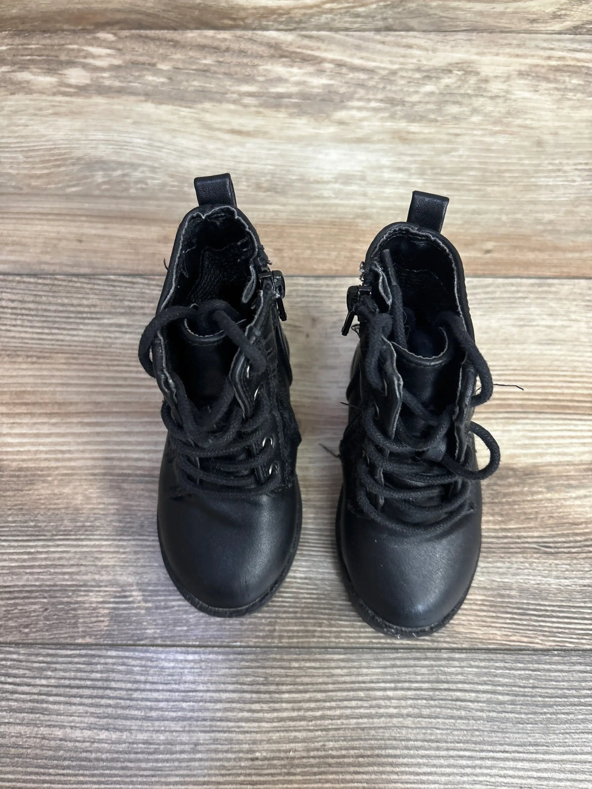 Pair of black toddler boots with laces and zippers on wooden floor in kids resale store