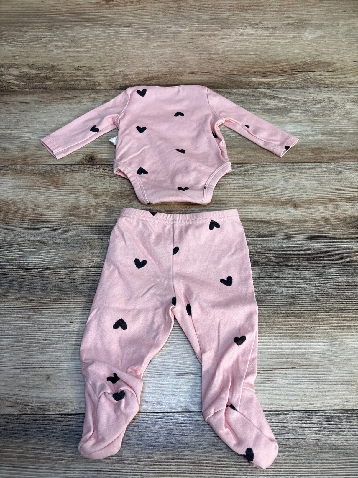 Pink baby outfit set with long sleeve onesie and footed pants, black heart print, on wood background