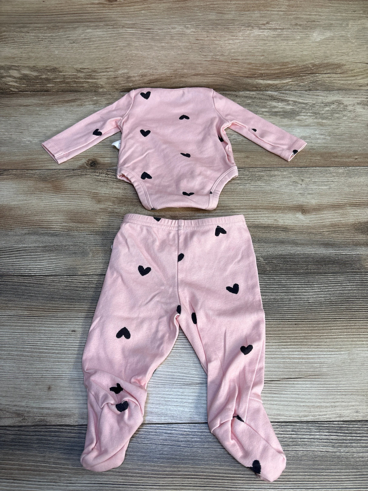 Pink baby outfit set with long sleeve onesie and footed pants, black heart print, on wood background