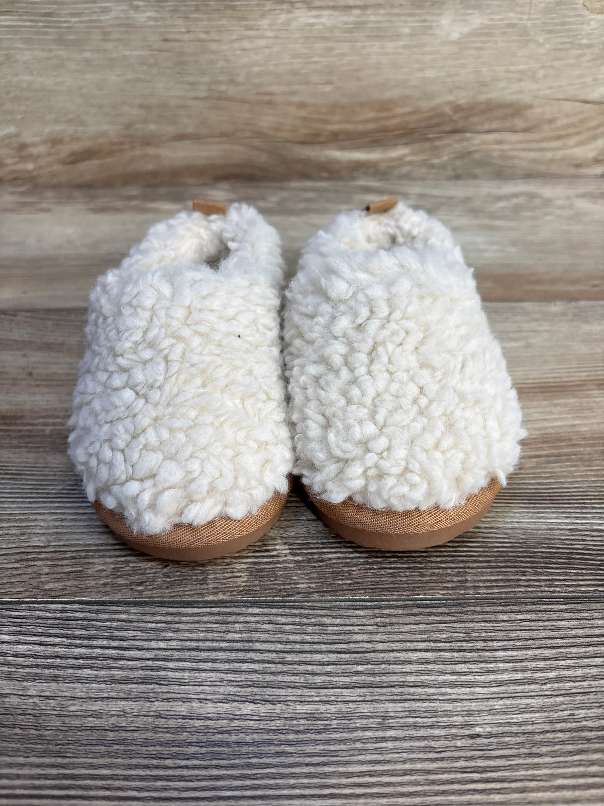 cozy white sherpa baby booties with tan soles on wooden background