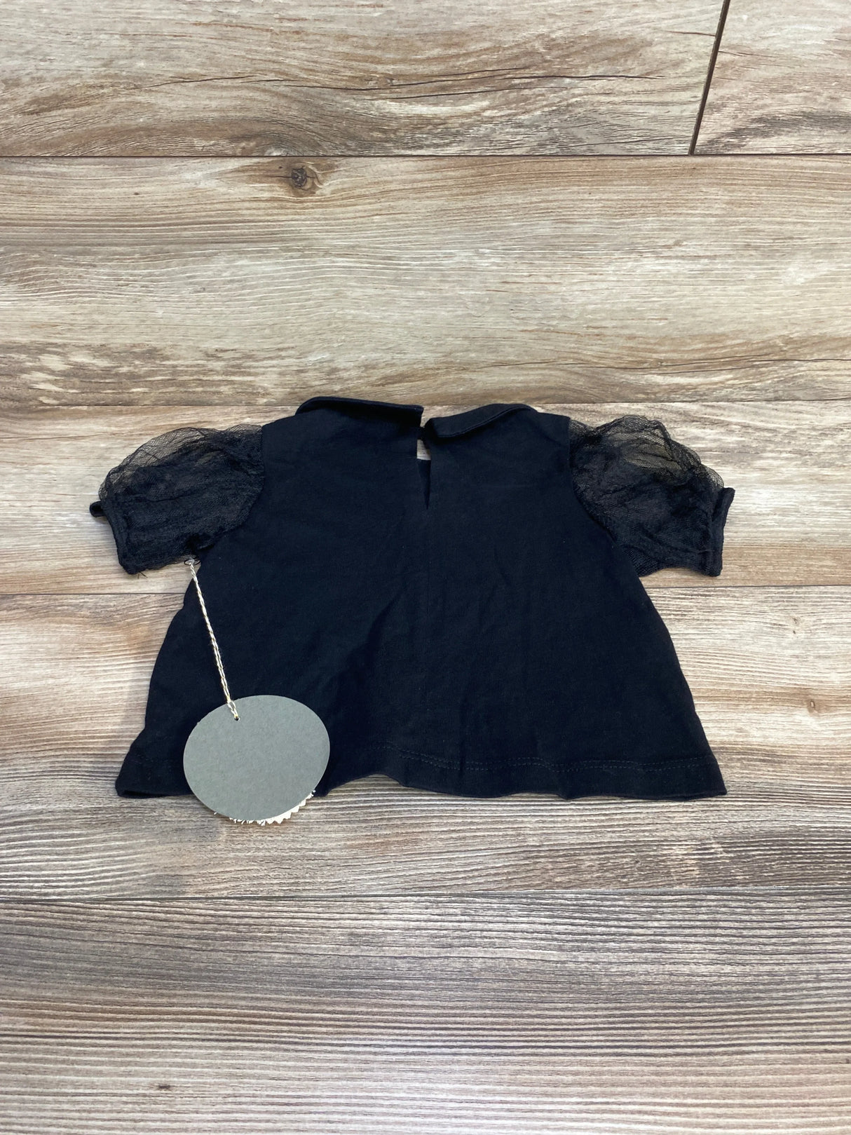 Flat lay of black tulle puff sleeve toddler top showcasing sheer puff sleeves and keyhole back closure with light wood background