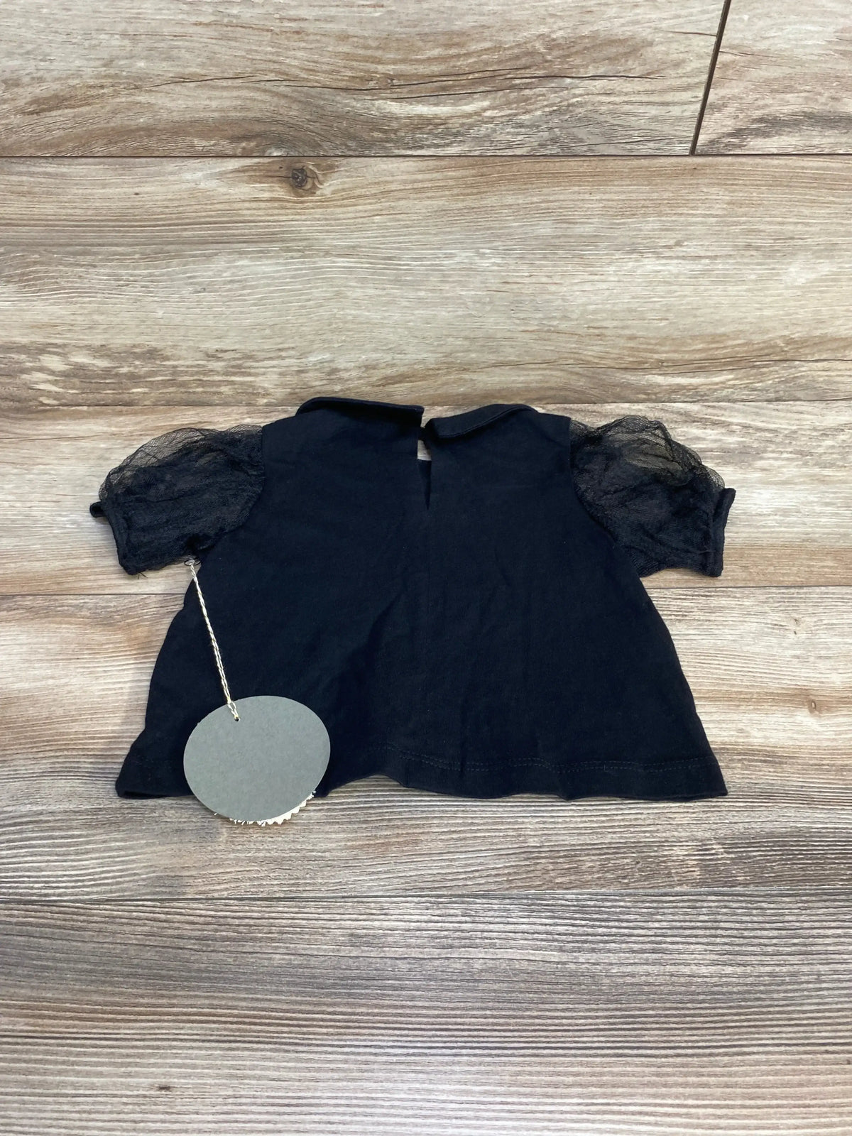 Flat lay of black tulle puff sleeve toddler top showcasing sheer puff sleeves and keyhole back closure with light wood background