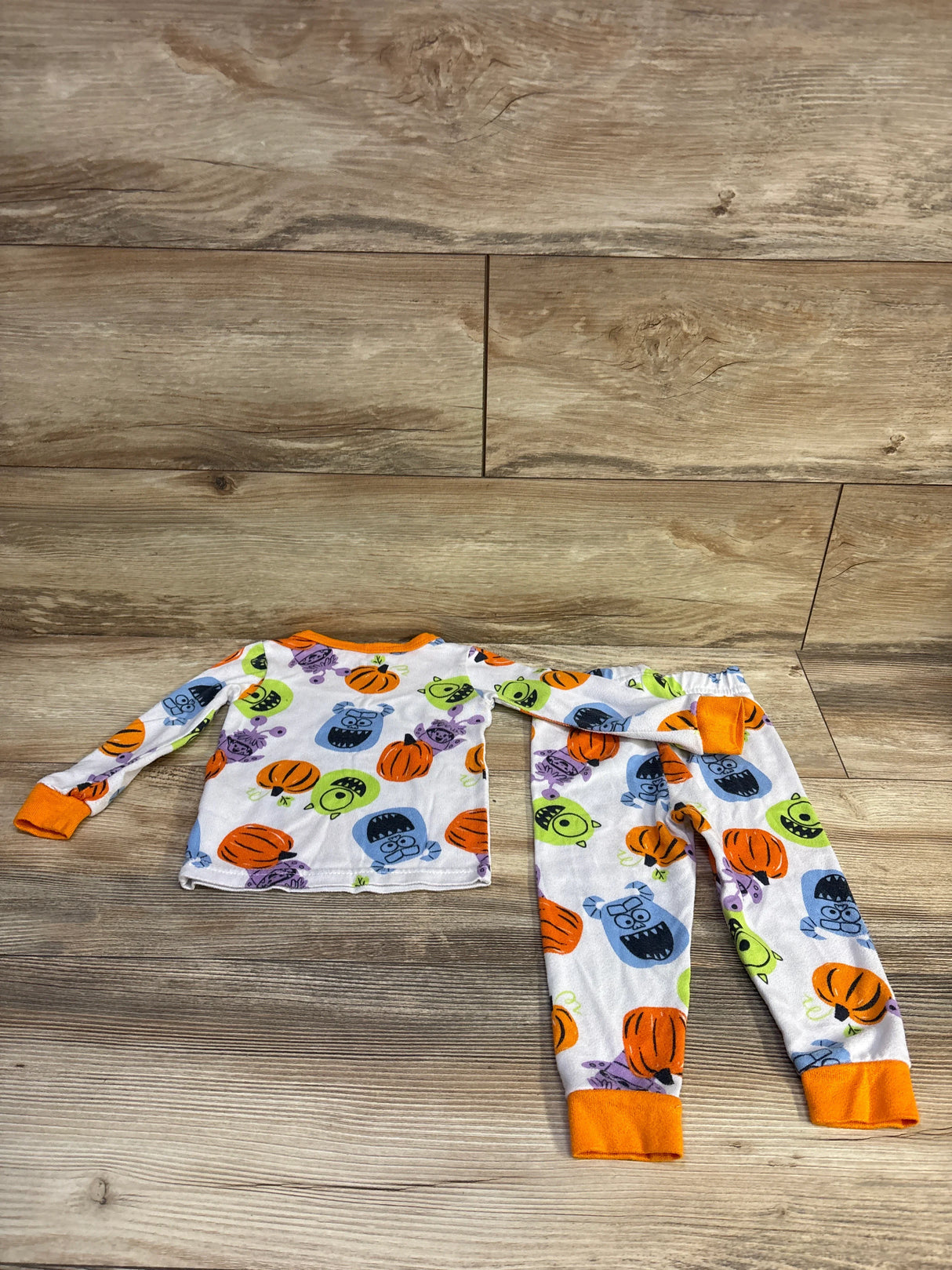 Flat lay of Disney Monsters, Inc 2-piece pajama set size 2T showcasing pumpkin faces and orange cuffs on wood background