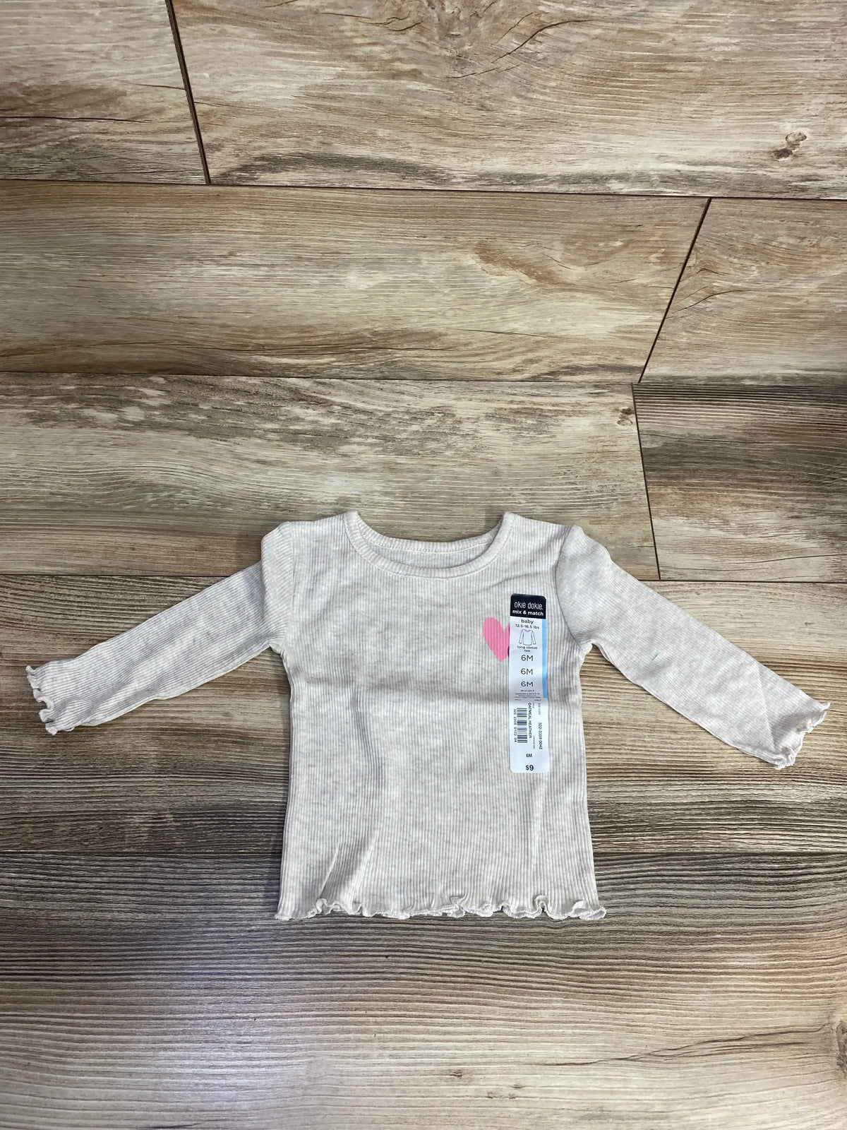 Gray ribbed long-sleeve baby shirt with ruffled edges and pink heart design, size 6 months, on wood floor