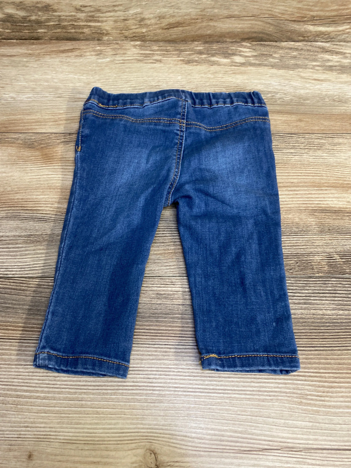 Flat lay of H&M blue baby jeggings (3–6 months) showing back view with elastic waistband and straight legs on wood background