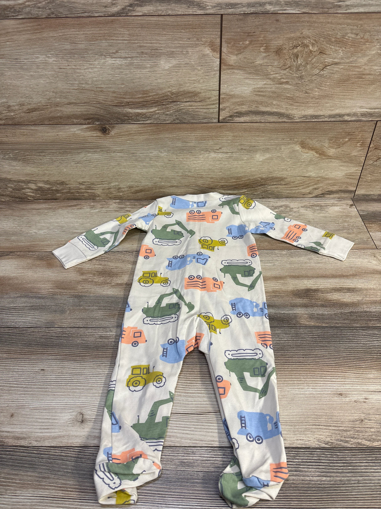Flat lay of Child of Mine footed sleeper showcasing multicolor construction vehicle print on beige fabric with wood background