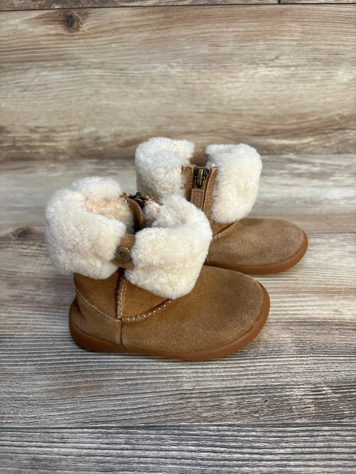 Side view of UGG Ramona boots in chestnut suede with folded white shearling cuff and visible zipper on wood background