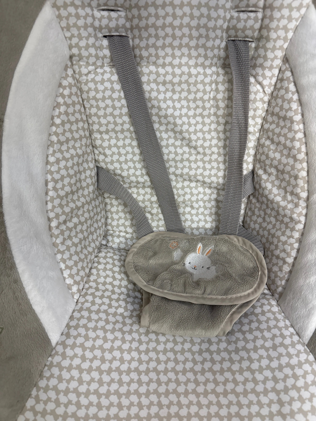 Top-down view of Ingenuity InLighten Cradling Swing seat showcasing gray harness straps, plush beige patterned fabric, and embroidered bunny crotch cover