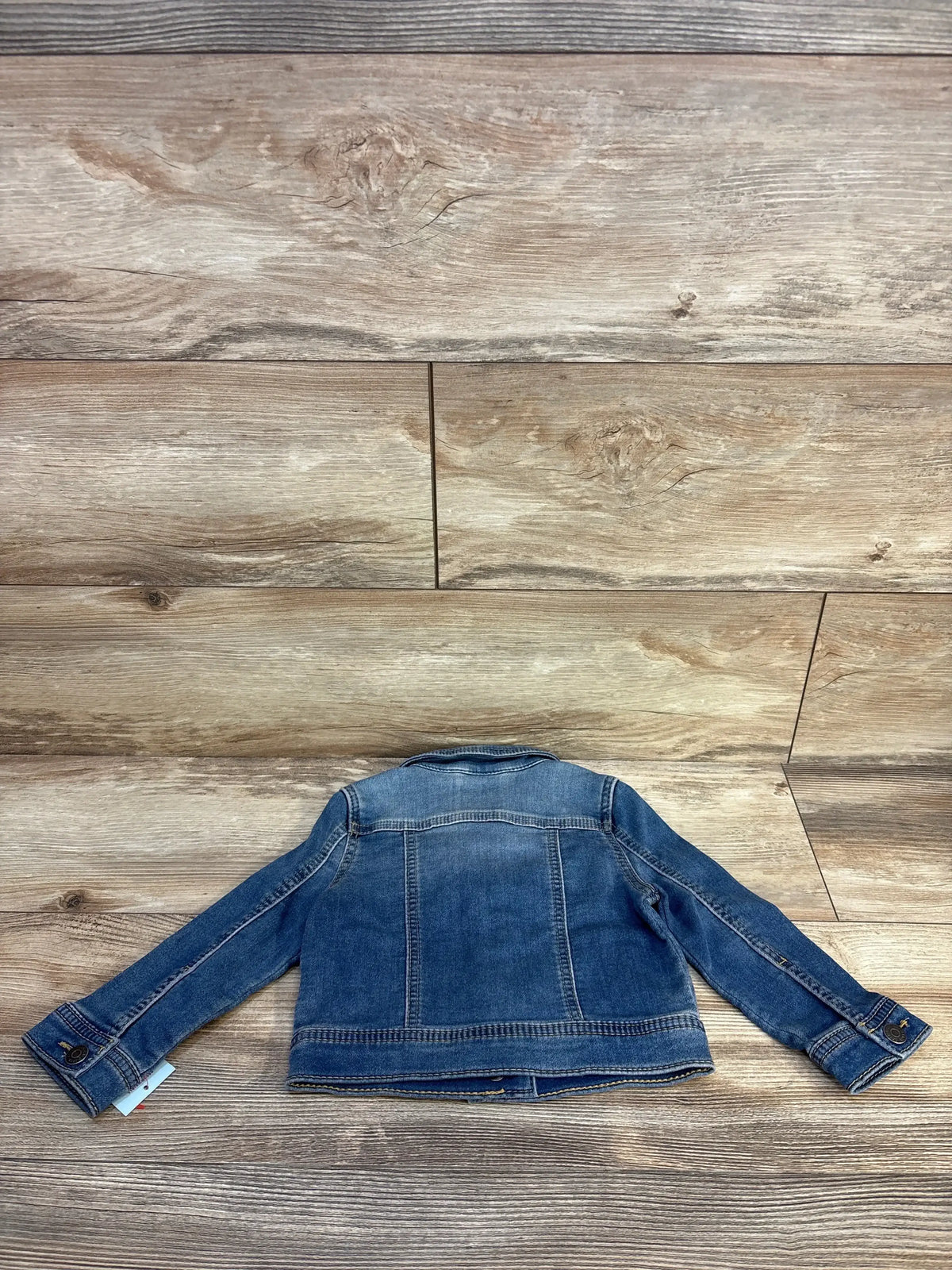 Back view of Cat and Jack toddler blue denim jacket showcasing stitched back yoke and buttoned cuffs on wood background