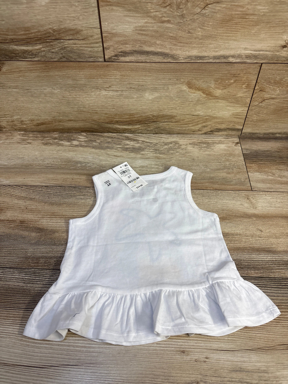 Back view of Epic Threads white peplum tank top, size 2T, showing ruffled hem and attached tag on wood floor background