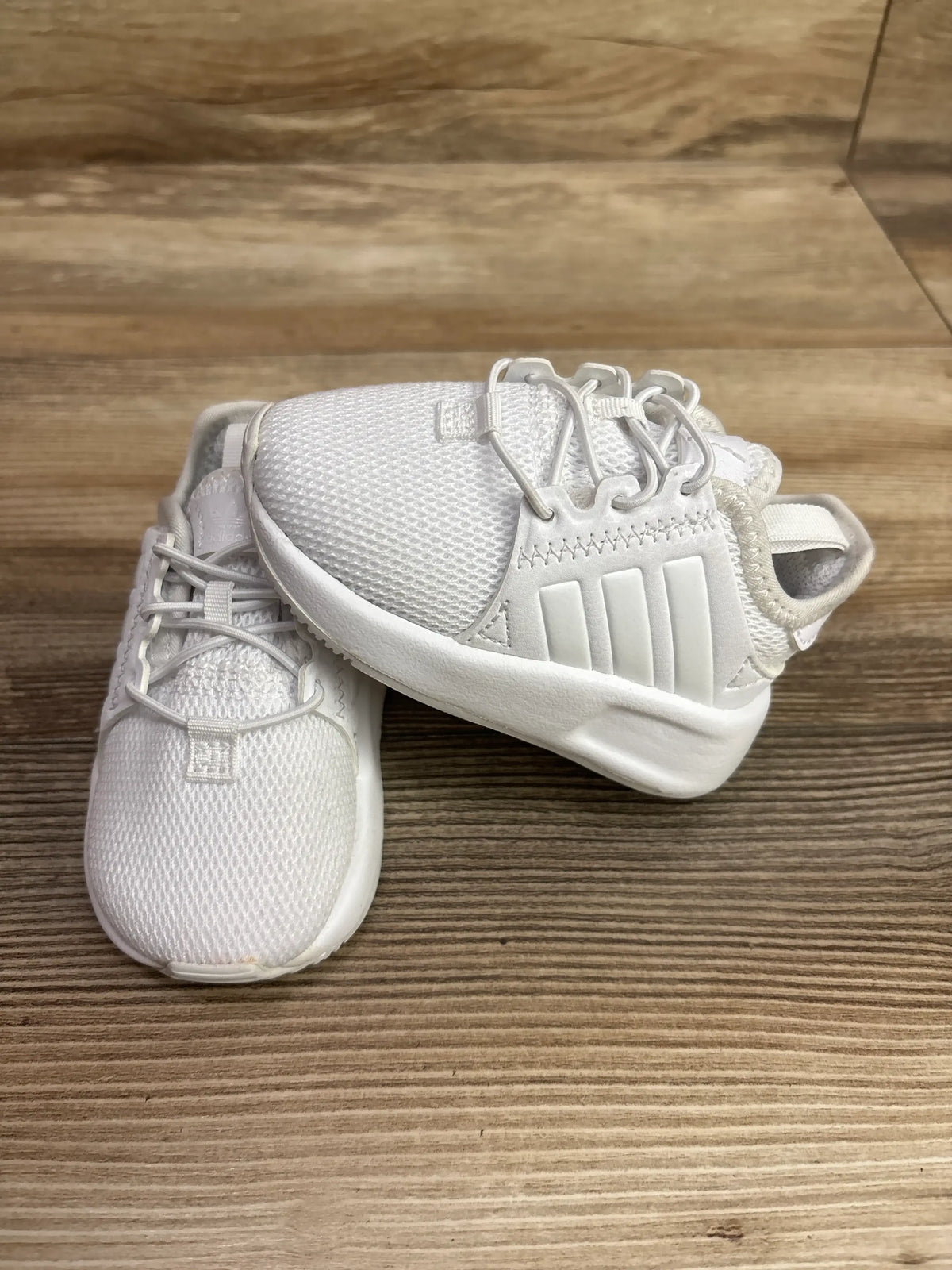 Top view of Adidas X_PLR sneakers showcasing white mesh uppers, laces, and three stripes on a wood floor