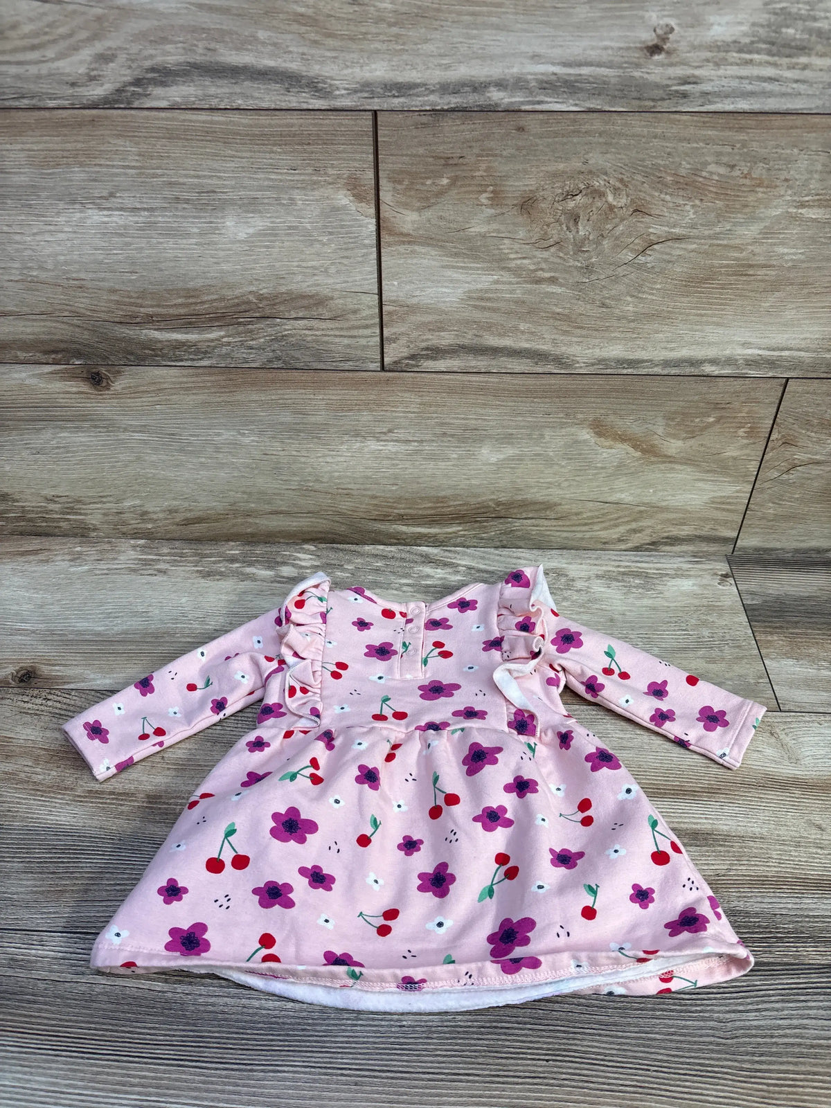 Front view of pink cherry print sweatshirt dress showcasing long sleeves and ruffled shoulders with a wood plank background
