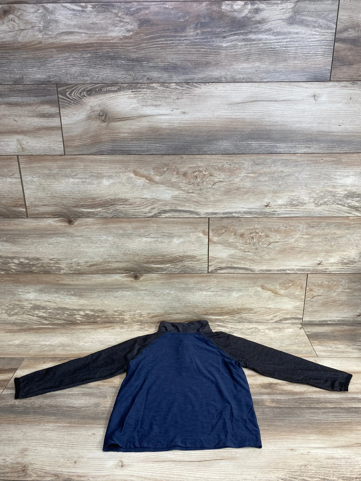 Blue and black long-sleeve kids quarter-zip shirt laid flat on wooden floor